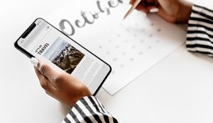 A close up of a women's hands holding an iPhone in one hand and writing on an October calendar with the other